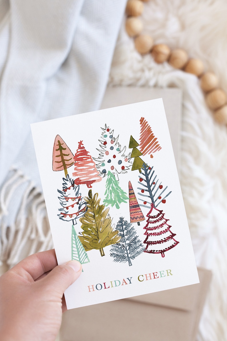 May include: A white card with a festive illustration of colorful Christmas trees and the text "HOLIDAY CHEER".
