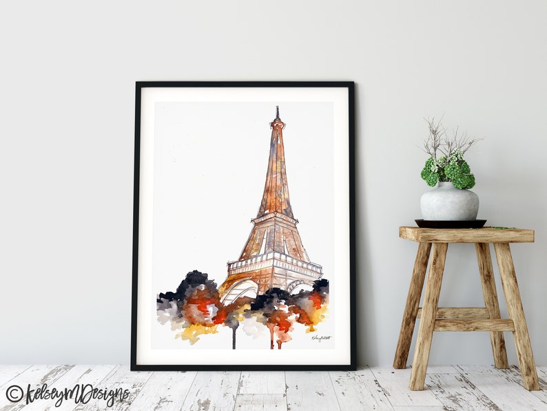 May include: A watercolor painting of the Eiffel Tower in Paris, France. The tower is depicted in shades of brown and orange, with a white background. The painting is framed in a black frame.