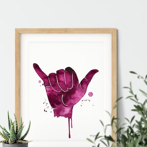 May include: A watercolor painting of a pink hand making the shaka sign, a popular Hawaiian gesture of peace, aloha, and good vibes. The hand is painted in a dripping style, with pink watercolor splatters around it.