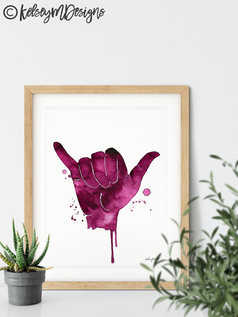 May include: A watercolor painting of a pink hand making the shaka sign, a popular Hawaiian gesture of peace, aloha, and good vibes. The hand is painted in a dripping style, with pink watercolor splatters around it.