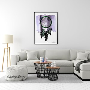 May include: A watercolor painting of a dreamcatcher with green and white details hanging from a purple background. The dreamcatcher is surrounded by a black frame.