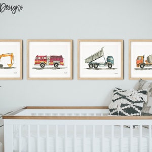May include: Four framed watercolor prints of construction vehicles: an excavator, a fire truck, a dump truck, and a cement mixer. The prints are in light wood frames and are displayed above a white crib. The artist's name, kelseymdesigns, is in the top left corner.