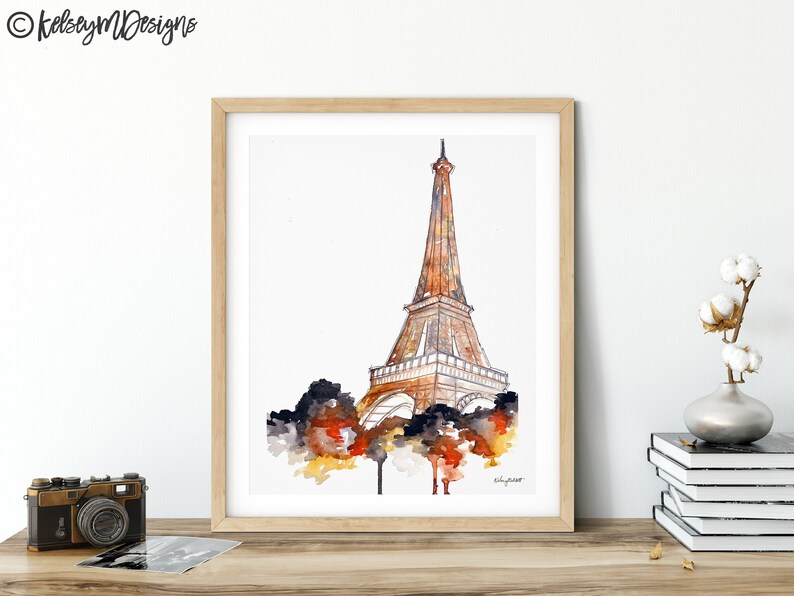 May include: A watercolor painting of the Eiffel Tower in Paris, France. The tower is depicted in shades of brown and gold, with a white background. The painting is framed in a light wood frame.