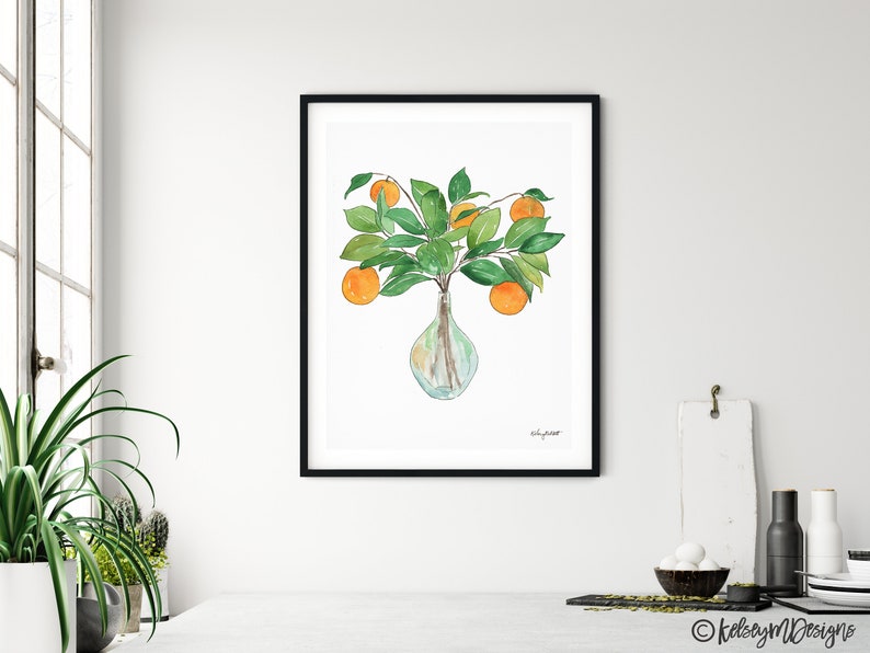 May include: A watercolor painting of a vase filled with orange blossoms and green leaves. The vase is clear glass and has a round shape. The painting is framed in black.