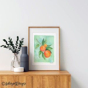 May include: A framed watercolor painting of a branch of oranges with green leaves on a light blue background.