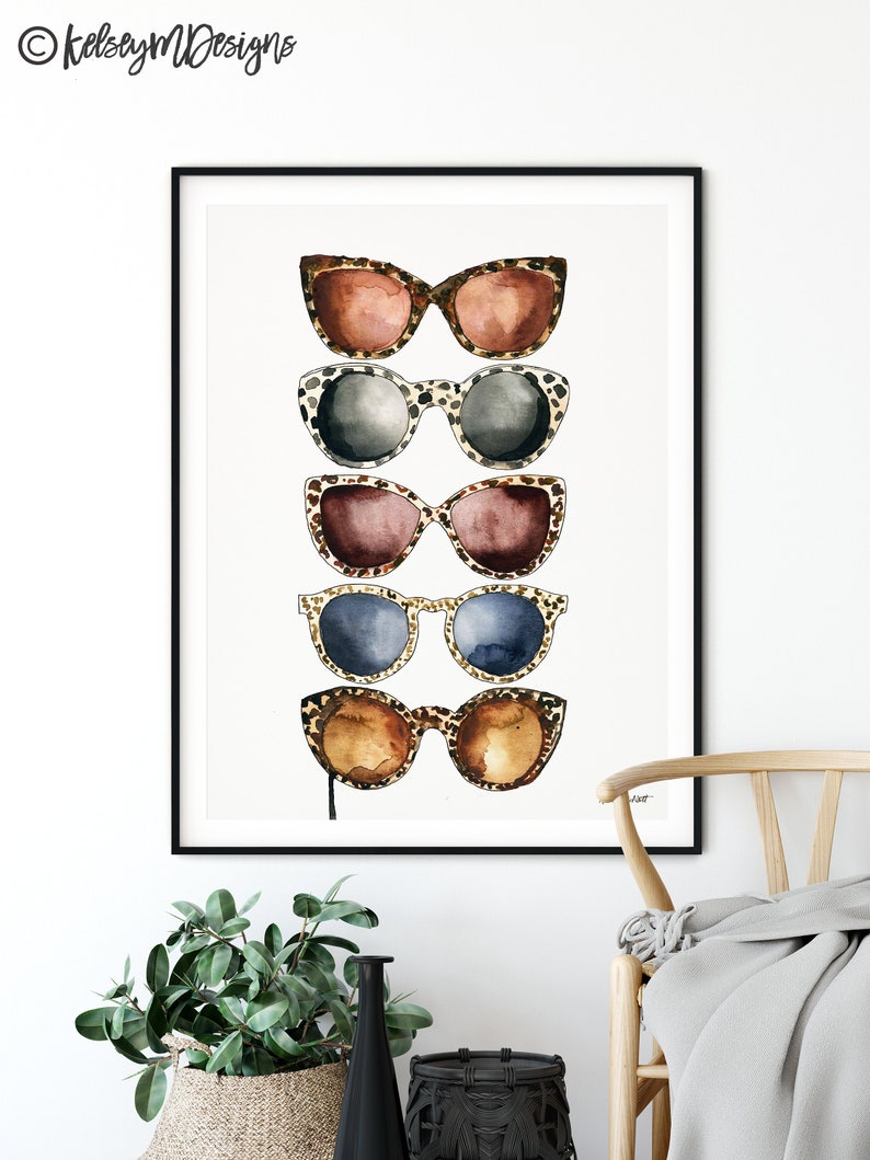 May include: A framed print of five pairs of sunglasses with leopard print frames. The sunglasses are stacked vertically, with the top pair being brown, the second pair being gray, the third pair being maroon, the fourth pair being blue, and the bottom pair being brown.