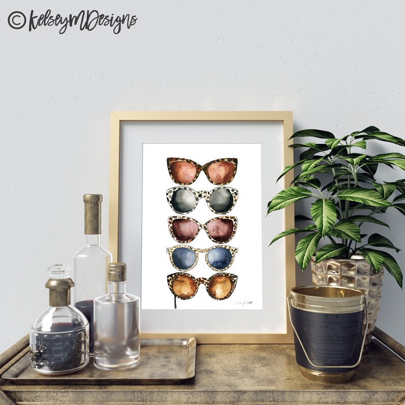 May include: A framed print of five pairs of sunglasses with leopard print frames. The sunglasses are stacked vertically and are in various colors, including brown, black, and blue.