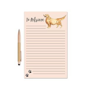 Może przedstawiać: Notatnik z napisem "To-Retrieve" i akwarelową ilustracją golden retrievera. Notatnik ma strony w linie i grafikę z odciskami łap. Złoty długopis z czarną końcówką rysika leży obok notatnika.