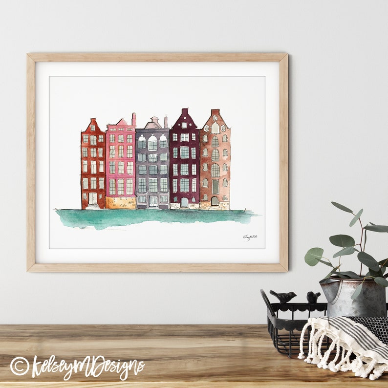May include: Watercolor painting of a row of five colorful buildings with windows and doors. The buildings are painted in shades of red, pink, purple, gray, and brown. The buildings are set against a light blue background with a green water line at the bottom.