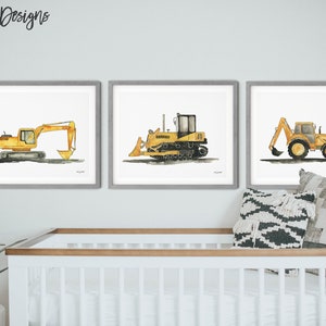 May include: Three watercolor paintings of yellow construction vehicles, including an excavator, bulldozer, and backhoe. The paintings are framed in gray frames and hung on a white wall above a white crib.