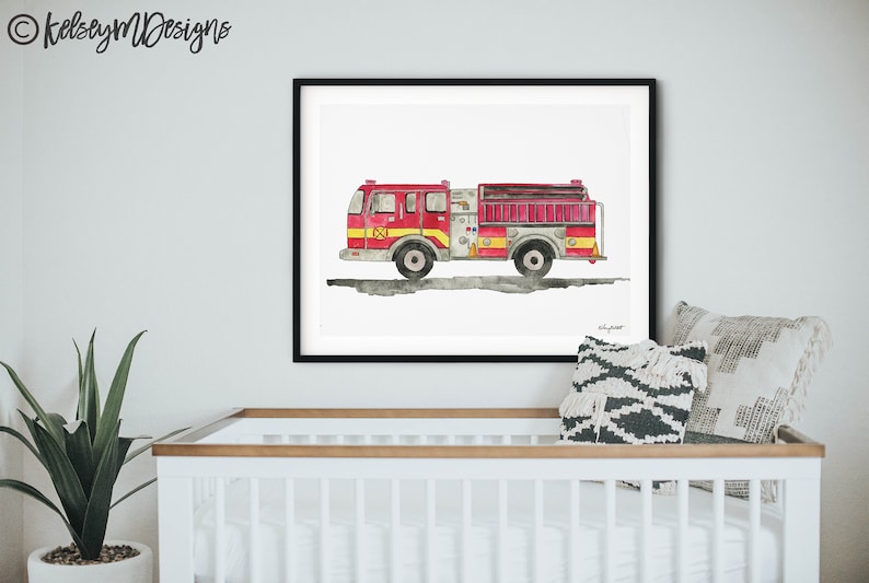 May include: Watercolor print of a red and yellow fire truck with black wheels, displayed in a black frame. The artwork is set against a white background. The print is hanging above a white crib.