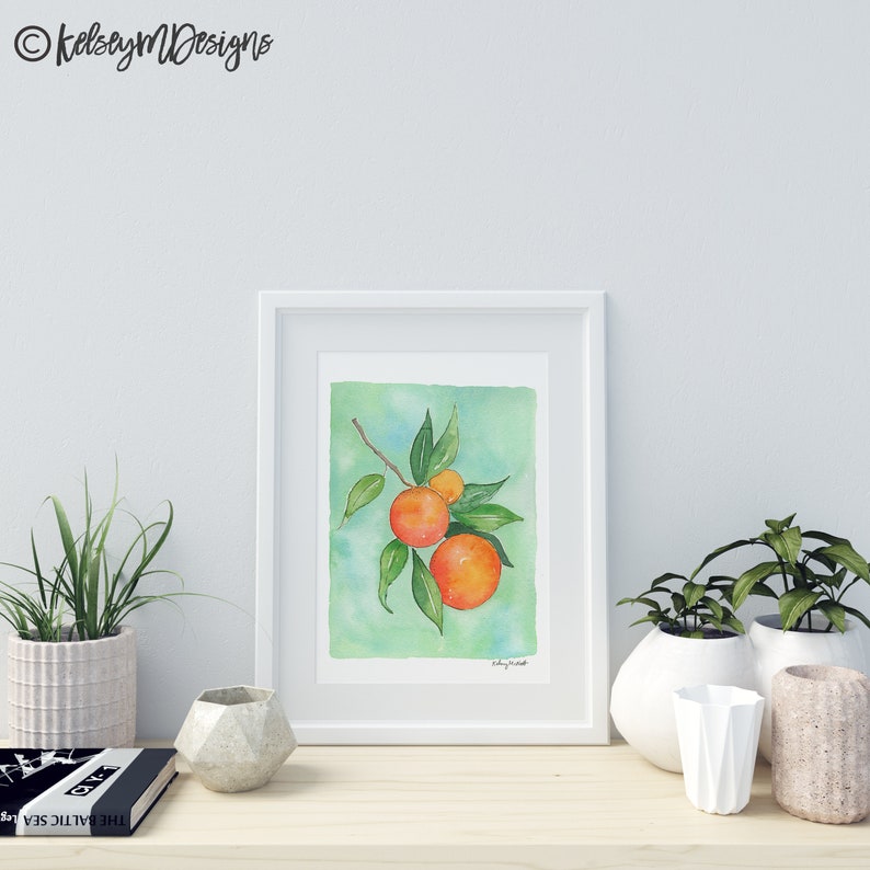 May include: A watercolor painting of a branch of oranges with green leaves on a light green background. The oranges are a vibrant orange color with a hint of red. The painting is framed in a white frame.