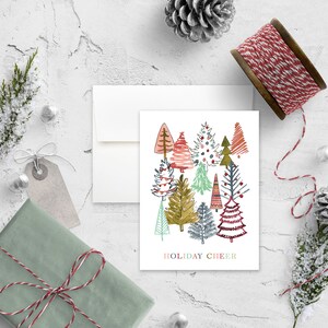 May include: A white card with a colorful illustration of a forest of stylized Christmas trees. The text "HOLIDAY CHEER" is printed at the bottom of the card.