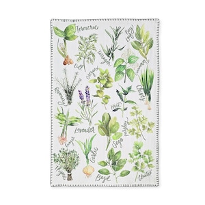 May include: A white rectangular kitchen towel with a black stitched border. The towel features watercolor illustrations of various herbs and spices, including turmeric, dill, rosemary, and lavender. Each herb is labeled with its name in a handwritten font.