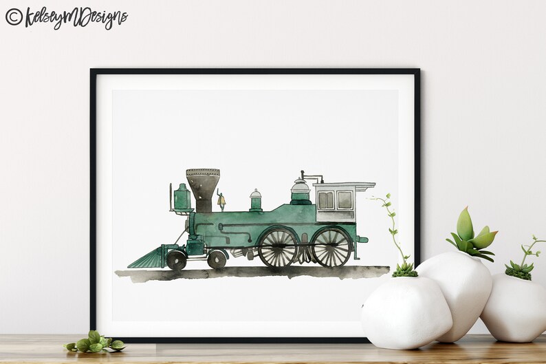 May include: Watercolor print of a vintage green steam train in a black frame. The train features a detailed design with black wheels and a smokestack. The artwork is signed "kelseymDesigns" in the top left corner. The print is displayed on a white background.