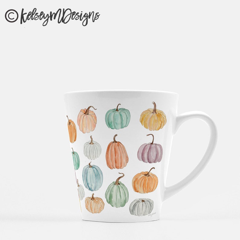 May include: White ceramic mug with a tapered design and a handle. The mug features a pattern of colorful pumpkins in various shades of orange, green, blue, and purple.