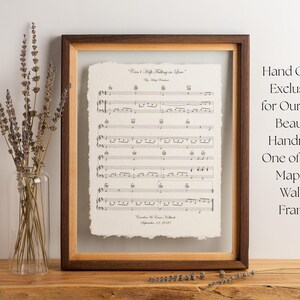 Peut inclure: Une partition encadr&eacute;e intitul&eacute;e Can't Help Falling in Love avec un bord effiloch&eacute;, dans un cadre en bois d'&eacute;rable et de noyer bicolore. L'impression pr&eacute;sente des notes de musique et du texte. Un vase en verre transparent contient de la lavande.