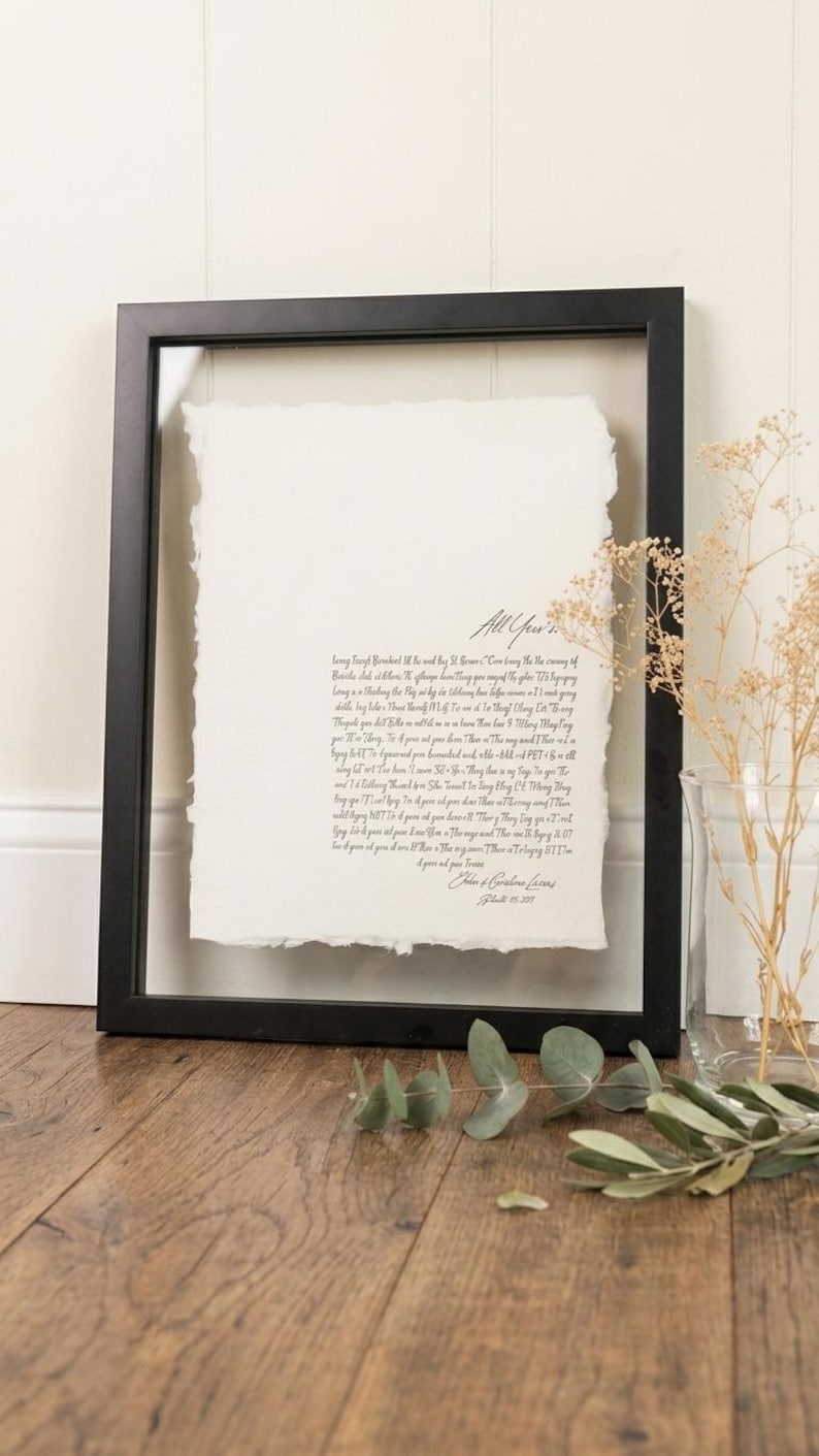 May include: A framed artwork featuring a handwritten script on textured paper. The black frame surrounds the paper, which has a deckled edge. The text includes the words "All Yours". The artwork is displayed on a wooden surface.
