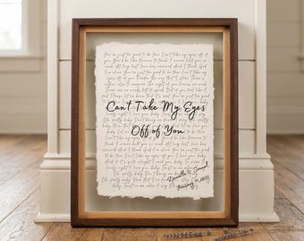 May include: A framed wall art piece featuring a cream-colored paper with deckled edges, displaying the lyrics to Can't Take My Eyes Off of You in black cursive script. The frame is dark brown wood with a deep inset, and the text includes a signature.