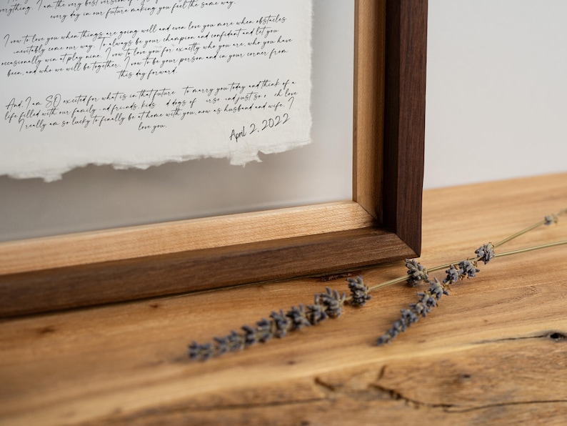 May include: A framed document featuring handwritten black cursive text on textured white paper with deckled edges. The frame is constructed from dark wood with a light wood inner border. The text includes the date April 2, 2022.