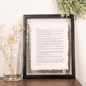 Könnte beinhalten: Ein schwarzer gerahmtes Bild mit weißem Hintergrund und einem getippten Brief im Inneren. Der Brief handelt von Liebe und Ehe. Das Bild steht auf einer Holzoberfläche mit einer Vase mit getrockneten Blumen davor.
