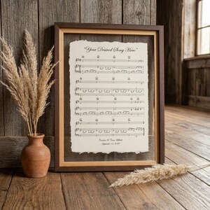 Peut inclure: Une impression encadr&eacute;e de partitions musicales avec le titre "Your Desired Song Here" imprim&eacute; en haut. Le papier pr&eacute;sente un bord effiloch&eacute; et inclut le texte "Caroline & Connor Millard" et "September 12, 2020" en bas, dans un cadre en bois sombre.