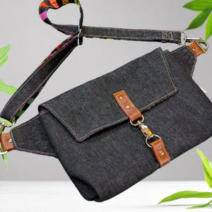 May include: A dark denim fanny pack with a flap closure and brown leather accents. The adjustable strap features a colorful striped pattern. The bag has a silver clasp and stitching in multiple colors.