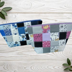 May include: Two patchwork zipper pouches. One is blue with dog paw prints and dog illustrations. The other is grey, pink, and purple with cat illustrations. Both have a rectangular shape and are made of fabric.
