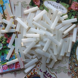 May include: A pile of small, translucent, white plastic tubes. The tubes are cylindrical with a hollow center. The background features vintage-style floral and perfume label ephemera.