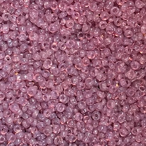 May include: A close-up view of a large quantity of small, translucent, light purple seed beads. The beads are round and have a hole in the center.
