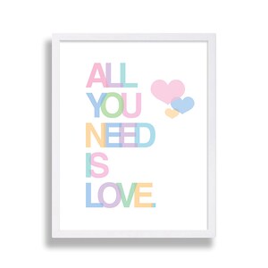May include: A white framed print with the text "ALL YOU NEED IS LOVE" in rainbow colors. The text is stacked vertically and the letters are overlapping. There are three hearts in the upper right corner of the print, one pink, one blue, and one yellow.