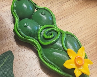 Könnte beinhalten: Grüne Tonskulptur einer weiblichen Figur mit einem stilisierten Blumendesign. Die Figur ist mit Brüsten und einem Spiralmuster am Bauch dargestellt. Die Blume ist gelb mit einer orangefarbenen Mitte.