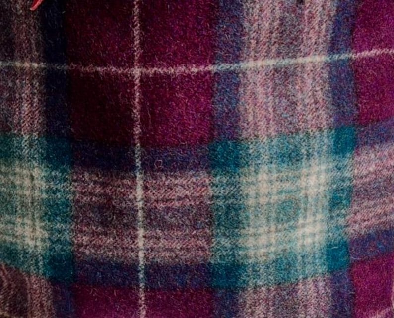 May include: A woven fabric featuring a plaid pattern with intersecting lines in shades of deep magenta, dark purple, teal, and white. The material has a soft, slightly fuzzy texture with a visible weave throughout the entire surface area.