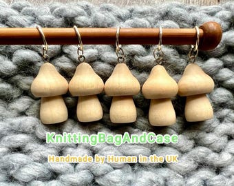 Puede incluir: Cinco colgantes de madera con forma de hongo colgados de una clavija de madera. Los colgantes son de color marrón claro con una parte superior redondeada y una base cilíndrica. El texto "KnittingBagAndCase" y "Handmade by Human in the UK" son visibles.