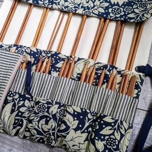 May include: A roll-up case with a blue and white floral pattern holds a collection of knitting needles. The case has a zippered pocket and a strap for carrying.