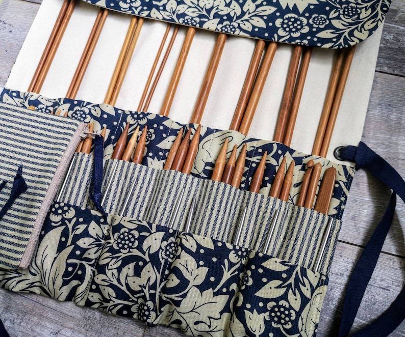 May include: A roll-up case with a blue and white floral pattern holds a collection of knitting needles. The case has a zippered pocket and a strap for carrying.