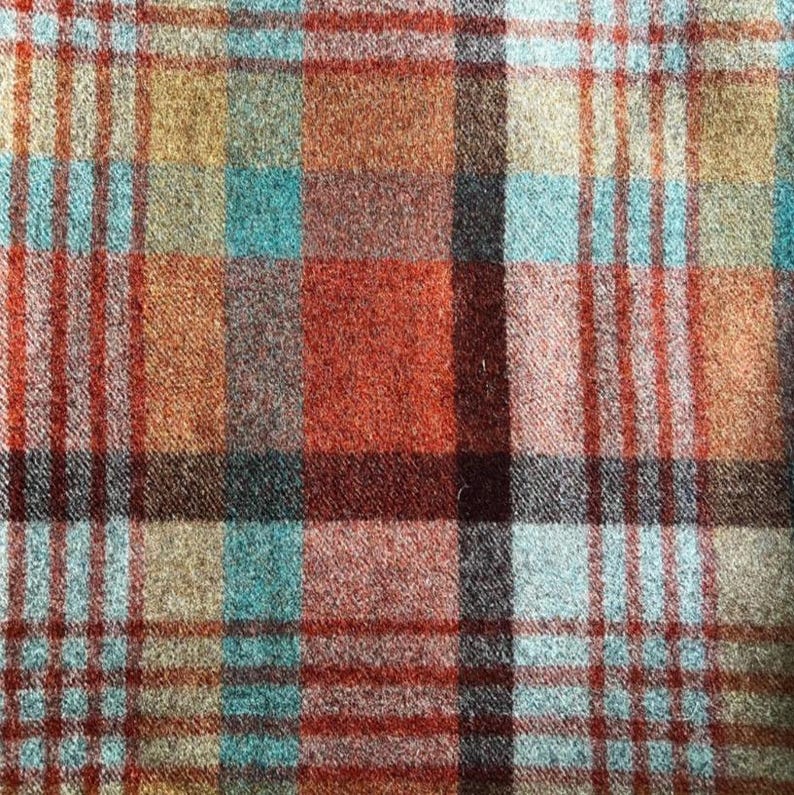 May include: A woven fabric featuring a multi-colored plaid pattern with intersecting lines in shades of burnt orange, deep red, light blue, and tan. The textile has a visible textured weave with a soft, slightly fuzzy appearance throughout.