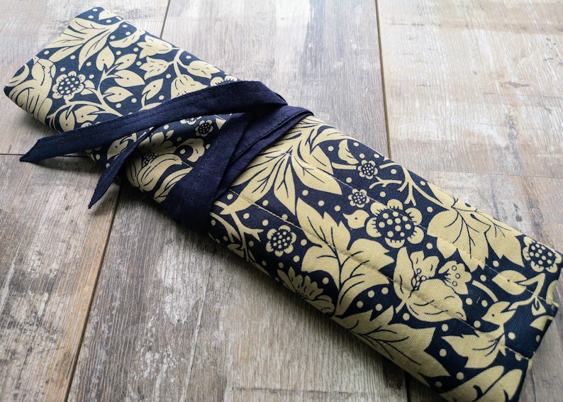 May include: A gold and navy blue fabric roll with a floral pattern, tied with a navy blue ribbon.
