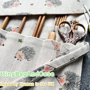 May include: A beige knitting needle case with a hedgehog pattern, holding wooden needles, a metal scissor, and two crochet hooks. The case is open, displaying the contents. The text "KnittingBagAndCase" is visible.