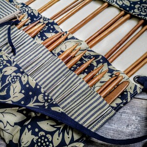 May include: A close-up of a fabric roll-up case with a blue and white striped pattern and a floral design. The case is filled with wooden knitting needles.