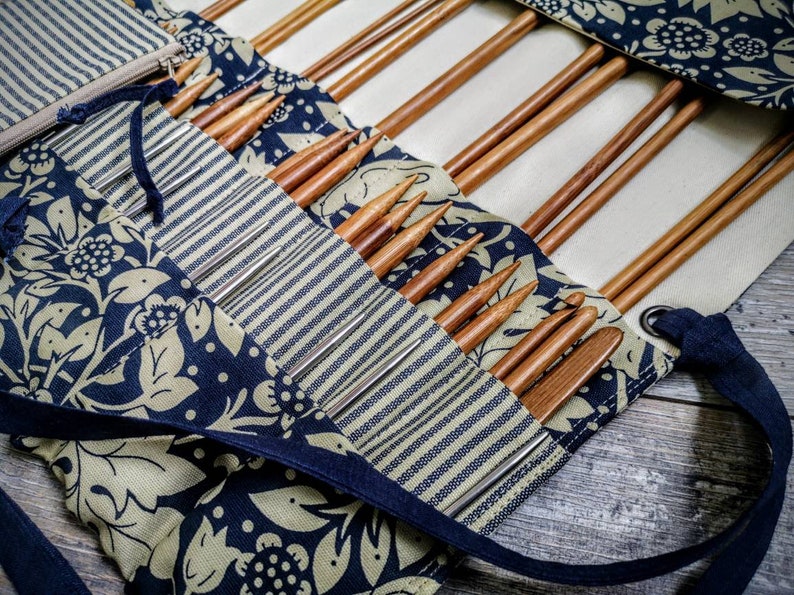 May include: A close-up of a fabric roll-up case with a blue and white striped pattern and a floral design. The case is filled with wooden knitting needles.