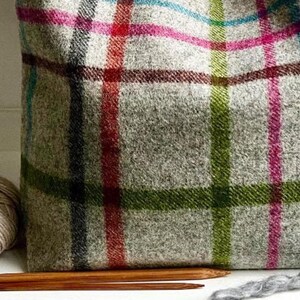 May include: A tote bag made of light gray wool fabric featuring a multi-colored plaid pattern with intersecting lines in shades of bright pink, lime green, turquoise, and dark red. The bag has a textured, woven appearance and a soft structure.