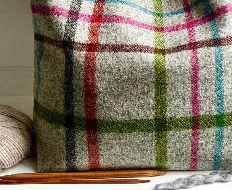 May include: A tote bag made of light gray wool fabric featuring a multi-colored plaid pattern with intersecting lines in shades of bright pink, lime green, turquoise, and dark red. The bag has a textured, woven appearance and a soft structure.