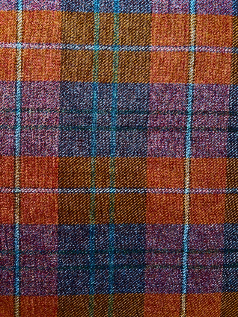 May include: A woven fabric featuring a plaid pattern with intersecting lines in shades of burnt orange, deep purple, and dark blue. The textile displays a diagonal twill weave texture with thin, light-colored vertical and horizontal stripes.