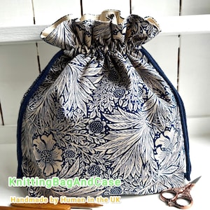 Op de afbeelding: Een trekkoordtas met een marineblauw bloemenpatroon op een crèmekleurige achtergrond. De tas heeft een marineblauw trekkoord en een marineblauwe rand. De tekst "KnittingBagAndCase" en "Handmade by Human in the UK" zijn zichtbaar.