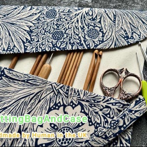 May include: A fabric knitting needle case with a blue and white floral pattern, holding wooden crochet hooks, needles, and scissors. The case is open, revealing the contents. The text "KnittingBagAndCase" and "Handmade by Human in the UK" is visible.