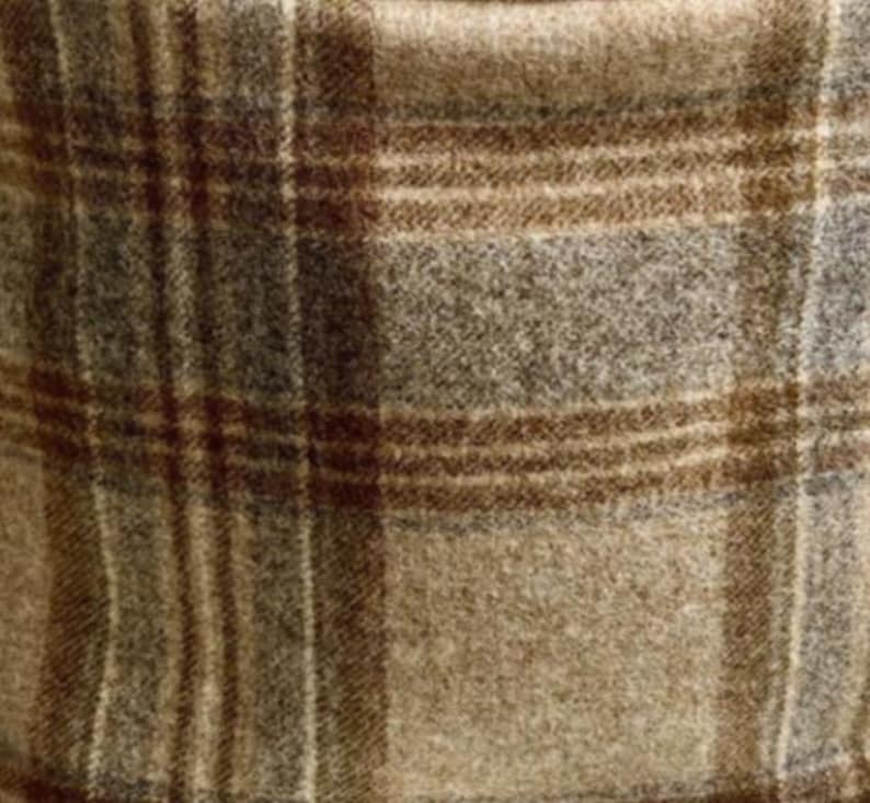 May include: A woven fabric featuring a classic plaid pattern in shades of tan, brown, and gray. The material has a soft, textured appearance with intersecting horizontal and vertical lines forming a grid across the surface of the textile.