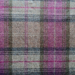 May include: A woven fabric featuring a plaid pattern with intersecting lines in shades of magenta, light gray, dark brown, and muted blue. The textile has a visible textured surface with a consistent weave throughout the entire material.