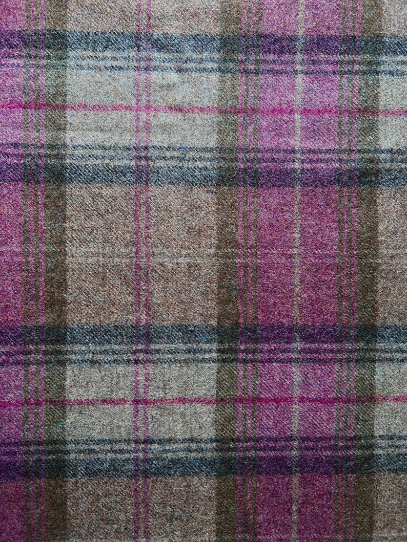 May include: A woven fabric featuring a plaid pattern with intersecting lines in shades of magenta, light gray, dark brown, and muted blue. The textile has a visible textured surface with a consistent weave throughout the entire material.