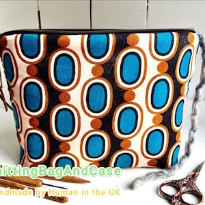 Könnte beinhalten: Eine rechteckige Stofftasche mit einem Retro-Muster aus blauen Ovalen und braunen Kreisen auf cremefarbenem Hintergrund. Die Tasche hat einen schwarzen Reißverschluss und einen braunen Lederzug. Der Text "KnittingBagAndCase Handmade by Human in the UK" ist sichtbar. Strickzubehör und eine Schere sind ebenfalls vorhanden.